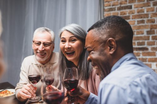 trois amis dégustant du vin ensemble : un homme blanc plus âgé, une femme asiatique et un homme noir d'âge moyen