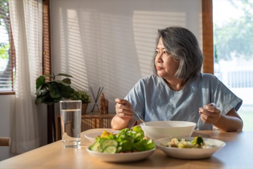grand-mère à la retraite reste à la maison avec un visage douloureux assis seul sur une table à manger dans la maison.